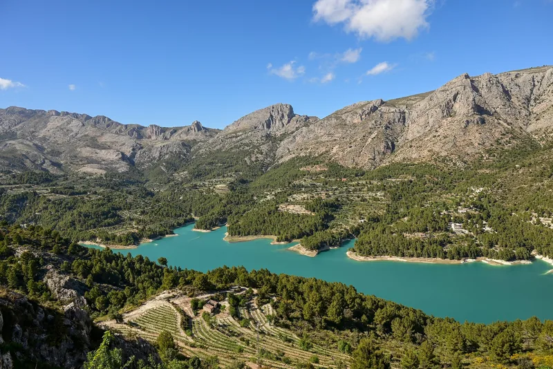 Turquoise Guadalest reservoir surrounded by wooded slopes and mountains
