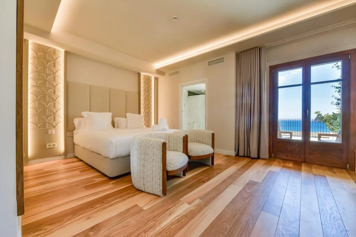 Suite bedroom with two armchairs and a sea-view terrace door at Las Torres